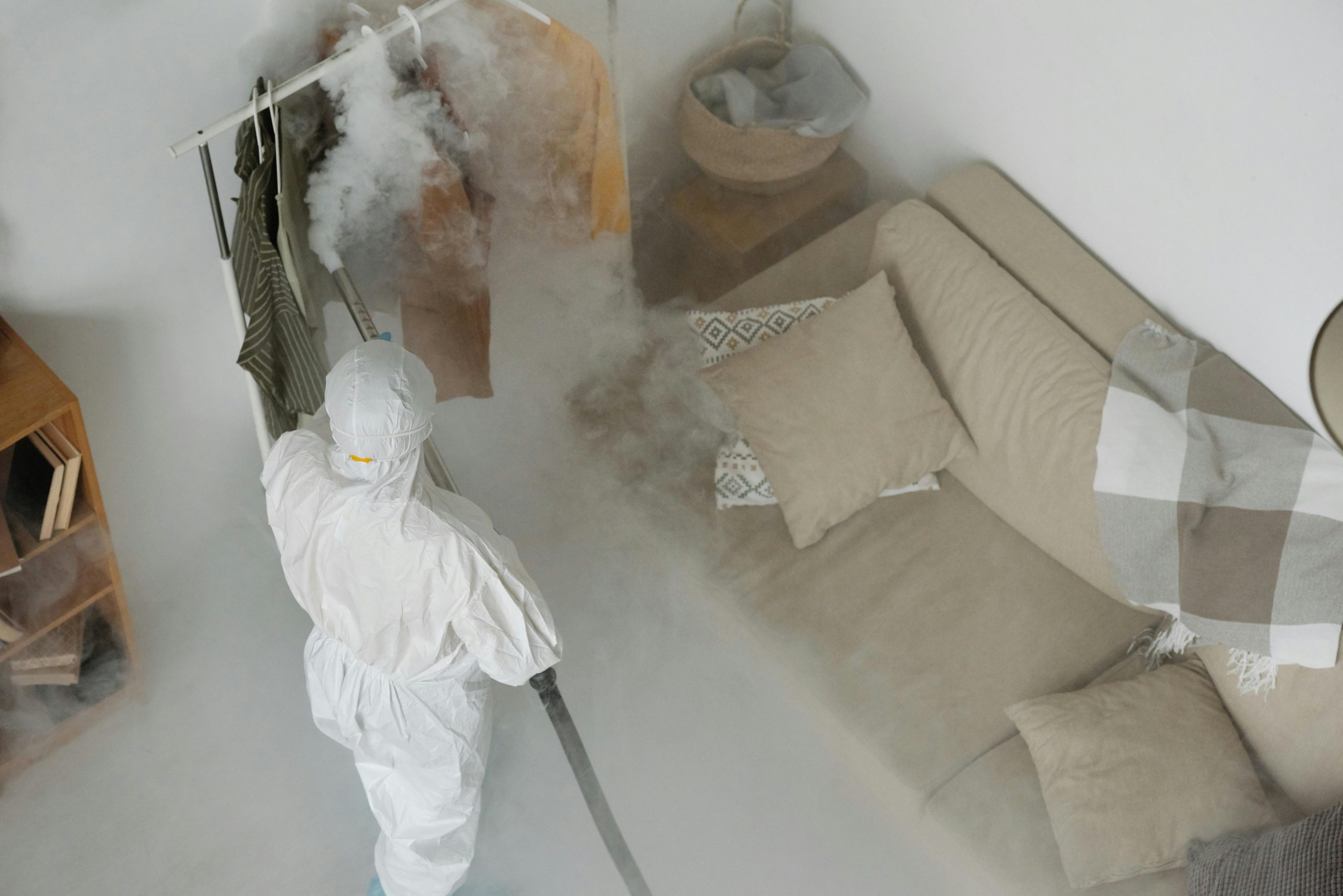 Professionnel équipé d’une combinaison de protection et d’un pulvérisateur effectuant une opération de désinfection dans un bâtiment.